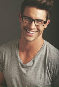 young man in grey shirt and glasses smiling | Porcelain Veneers